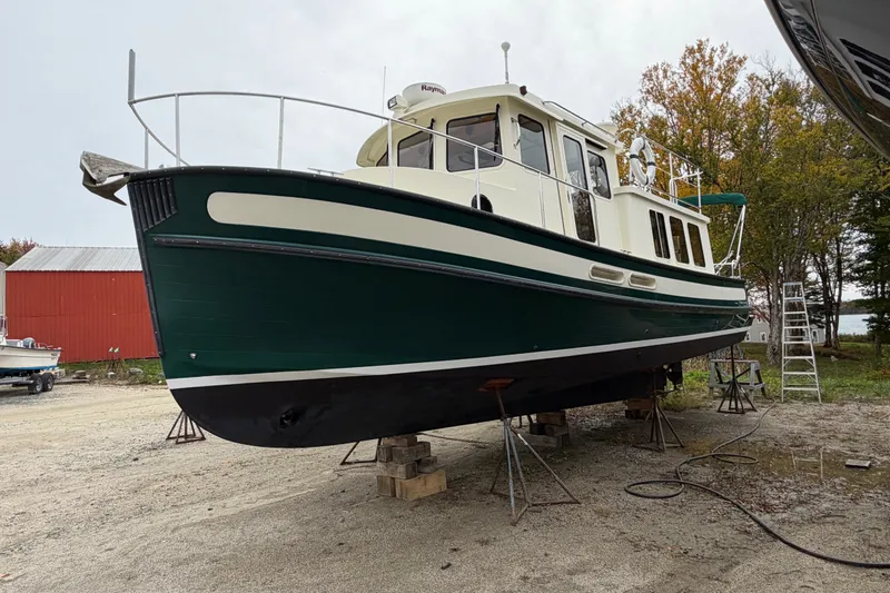 Slide: The Image of 2001 Nordic Tug 32 boat on dry dock, green and white hull, surrounded by trees and equipment. - 87