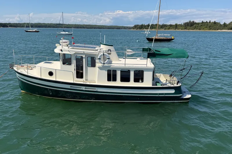 Slide: The Image of 2001 Nordic Tug 32 boat on calm water with sailboats in the background. - 4