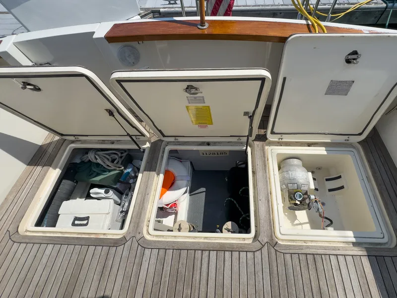Slide: The Image of The image shows the storage compartments on the deck of a 2002 Sabre 36 Express. Three open hatches reveal equipment and accessories. - 44