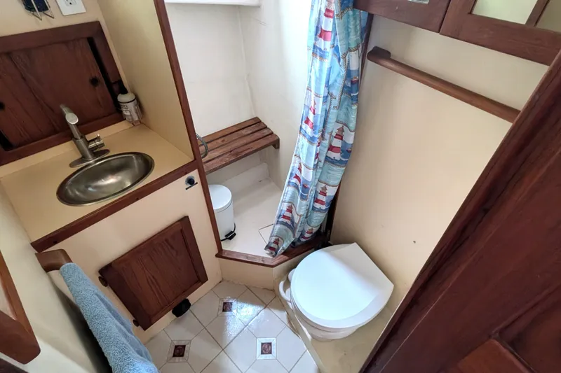 Slide: The Image of Bathroom interior of a 1993 Nordic Tug 32, featuring sink, toilet, and nautical-themed shower curtain. - 43