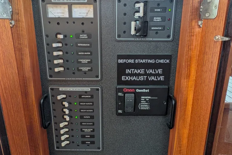 Slide: The Image of Electrical panel of a 2003 Nordic Tug 37 with various switches and Onan GenSet controls. - 27