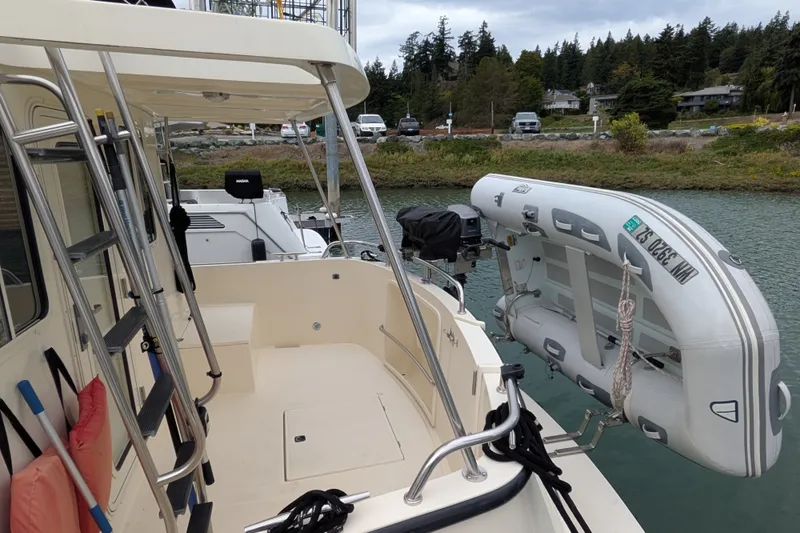 Slide: The Image of 2003 Nordic Tug 37 with dinghy, docked in a scenic marina setting. - 5