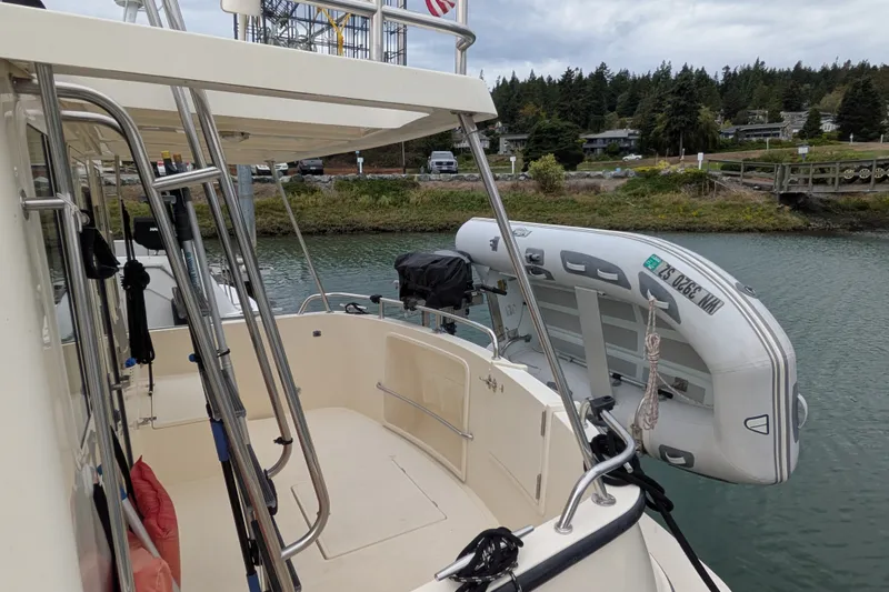 Slide: The Image of 2003 Nordic Tug 37 with dinghy on calm water, surrounded by lush greenery. - 4