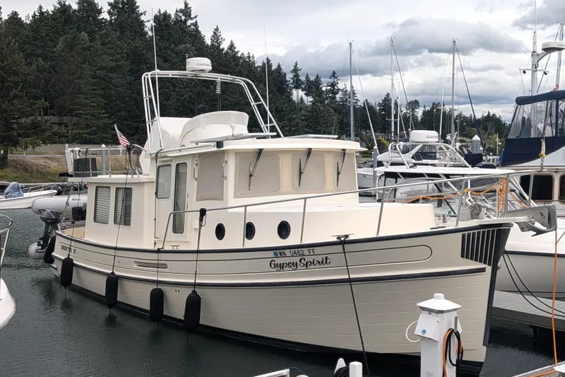 Slide: The Image of 2003 Nordic Tug 37 docked in a marina, surrounded by other boats and trees. - 2