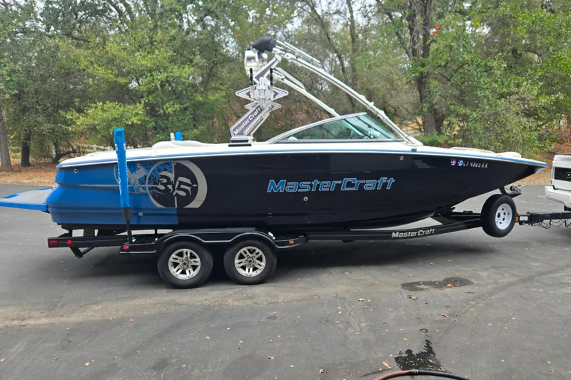 The Image of 2008 MasterCraft X-35 boat on trailer, parked outdoors with trees in background. - 1