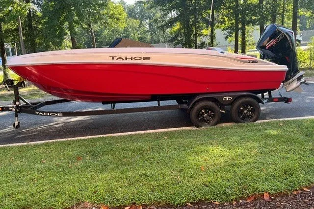 The Image of Red 2027 Tahoe T21 boat on trailer, parked on roadside with lush greenery. - 0