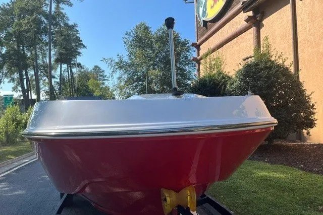 Slide: The Image of 2027 Tahoe T21 boat with red hull, parked outdoors near trees and building. - 3