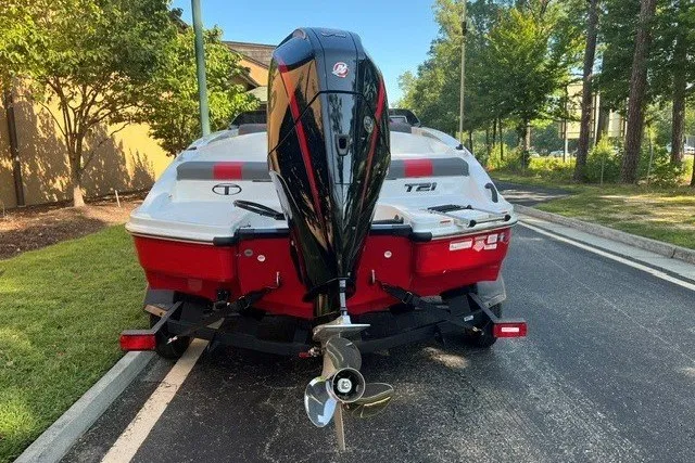 Slide: The Image of 2027 Tahoe T21 boat on trailer, rear view, parked on a tree-lined street. - 2