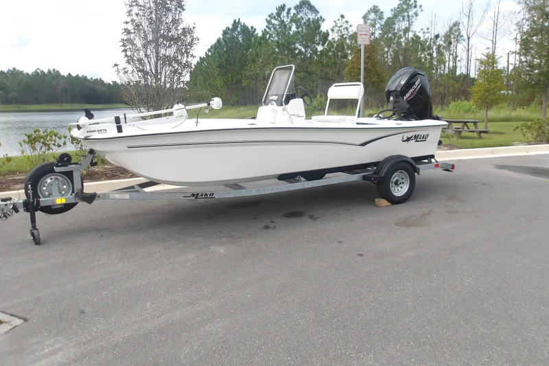 The Image of 2027 Mako Pro Skiff 17 CC boat on trailer near a lake, surrounded by trees. - 1