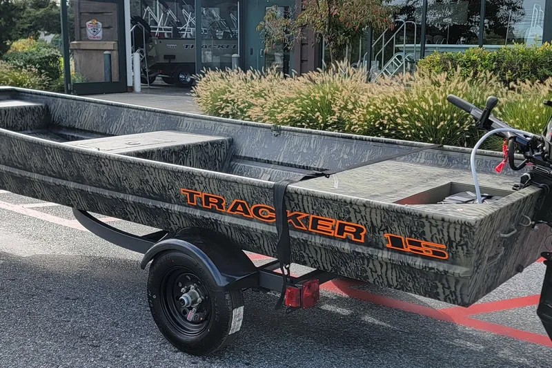 The Image of 2027 Tracker Grizzly 15 Jon boat on trailer, parked outdoors near greenery. - 0