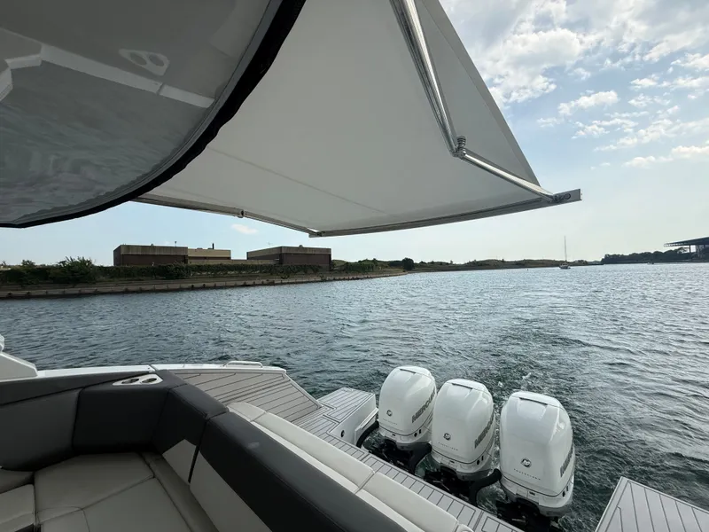 Slide: The Image of A luxury boat with three outboard engines, resting on calm water under a retractable sunshade. - 43