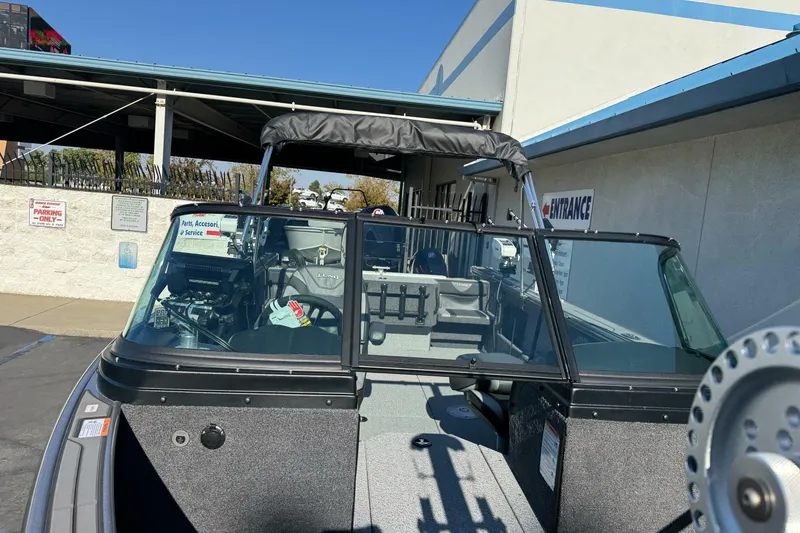 Slide: The Image of 2026 Lund 2075 Fisherman boat with canopy, parked near a service entrance. - 7
