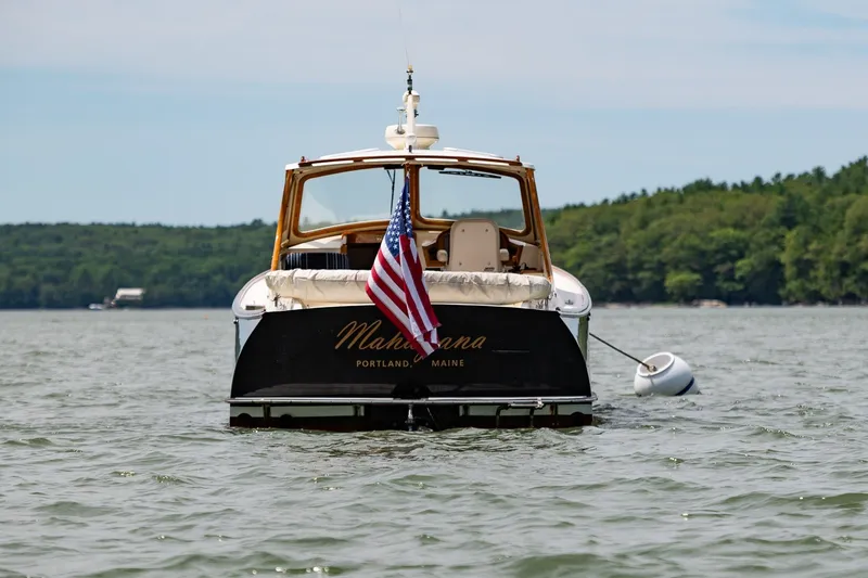 Slide: The Image of Hinckley Picnic Boat 36 Classic, 2000, on water with American flag, forested shoreline background. - 5