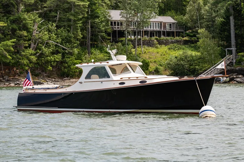 Slide: The Image of Hinckley Picnic Boat 36 Classic 2000 on water, surrounded by lush greenery and a lakeside cabin. - 3