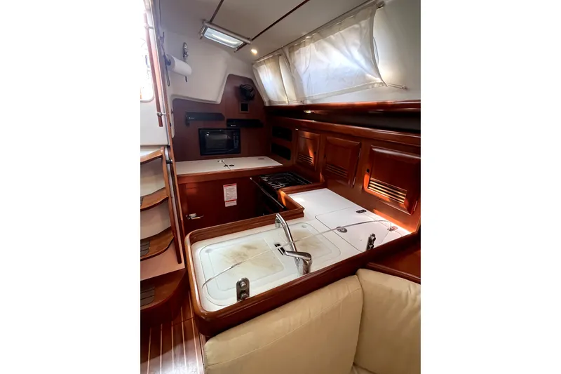 Slide: The Image of Interior of 2006 Beneteau Oceanis 393 yacht, featuring a compact kitchen with wooden cabinetry. - 27