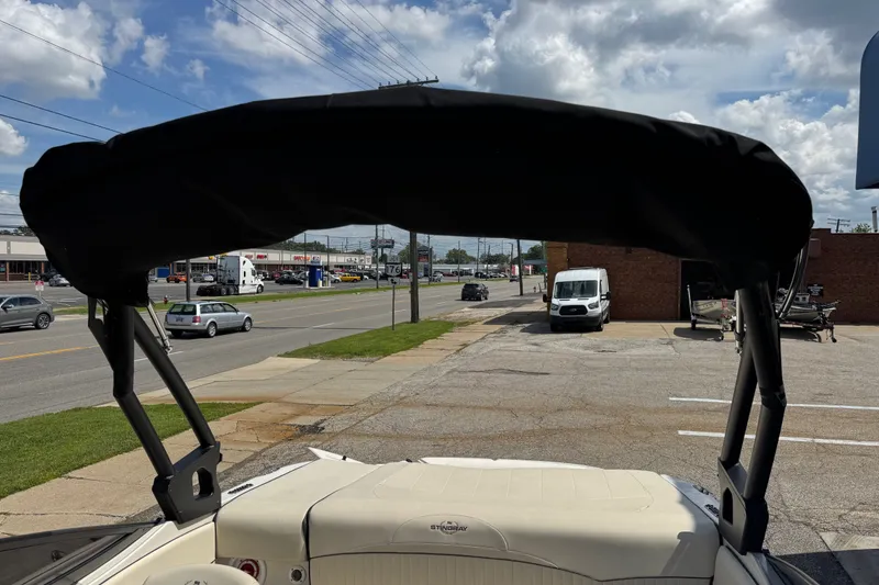 Slide: The Image of 2021 Stingray 208 LR boat with black canopy, parked near a busy street. - 24