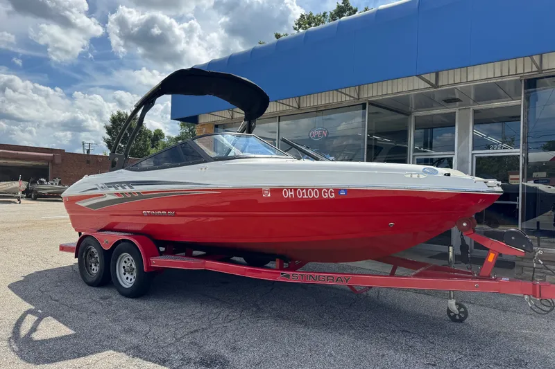 The Image of 2021 Stingray 208 LR boat on trailer, red and white, parked outside dealership. - 0