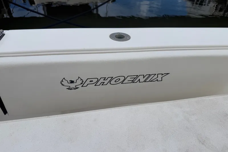 Slide: The Image of 1999 Phoenix 38 SFX Convertible boat logo on white surface, docked by water. - 16