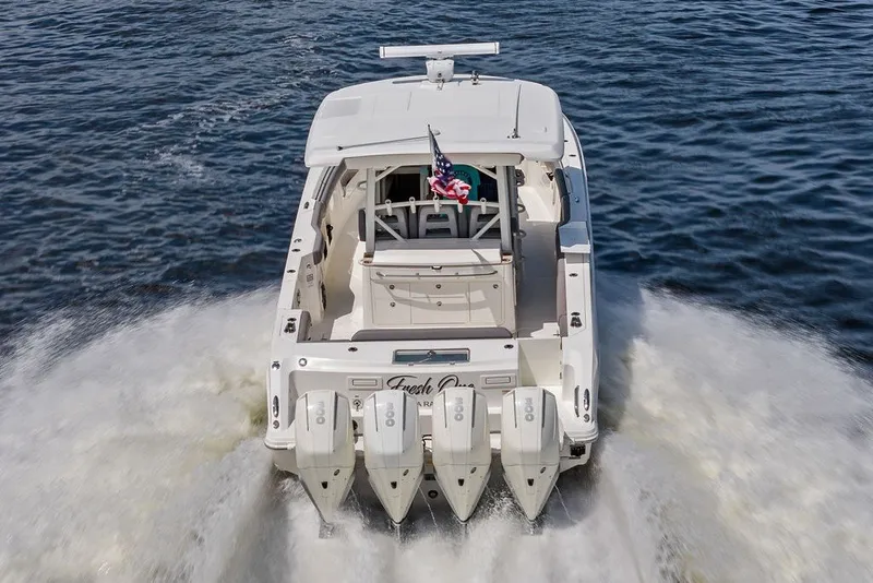 Slide: The Image of 2023 Boston Whaler 380 Outrage cruising on water, rear view with four engines. - 2