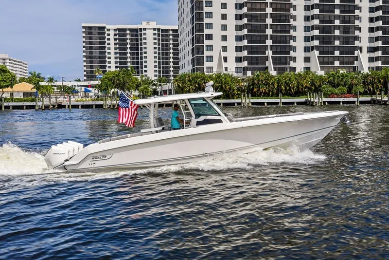 Slide: The Image of 2023 Boston Whaler 380 Outrage cruising on water near modern buildings. - 9