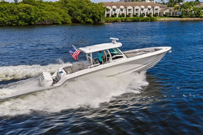 Slide: The Image of 2023 Boston Whaler 380 Outrage cruising on water with American flag, near waterfront homes. - 8