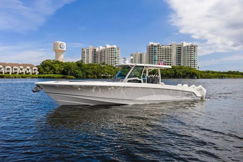 Slide: The Image of 2023 Boston Whaler 380 Outrage cruising on a scenic waterway with buildings in the background. - 14