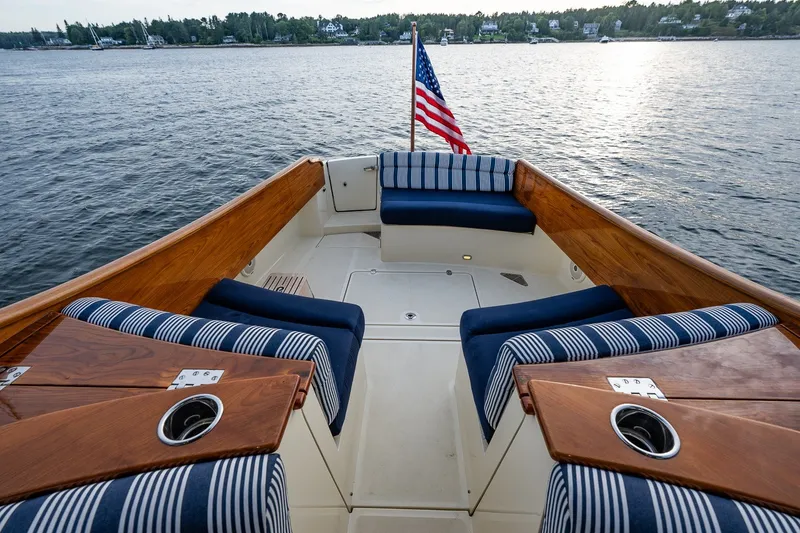 Slide: The Image of 2018 Hinckley Picnic Boat 34 MKII with striped seating, American flag, on calm water. - 13