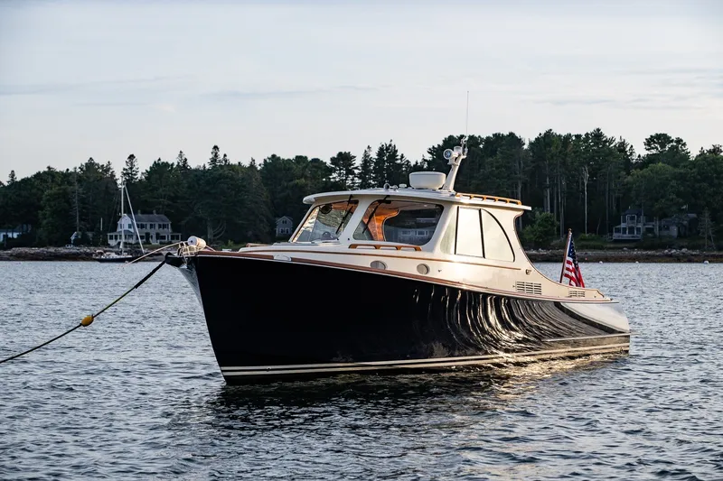 Slide: The Image of 2018 Hinckley Picnic Boat 34 MKII on calm water, surrounded by trees and houses. - 34