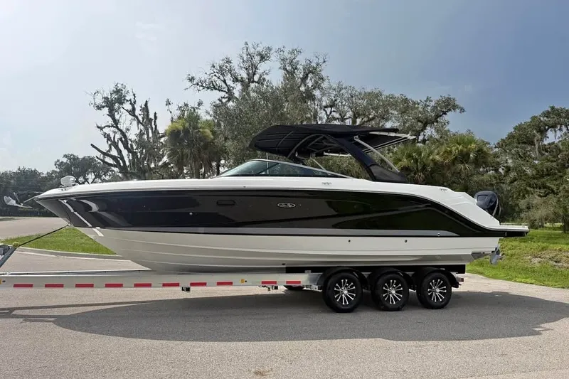 The Image of 2019 Sea Ray SLX 310 Outboard boat on trailer, parked on a road with trees. - 0