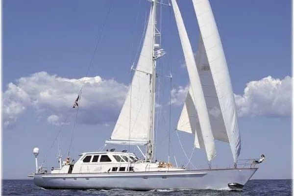 Slide: The Image of A white motorsailer cutter sails on calm water under a blue sky with white clouds. - 27