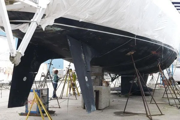 Slide: The Image of A large sailboat is propped up and undergoing maintenance. It is partially covered with a tarp. - 23
