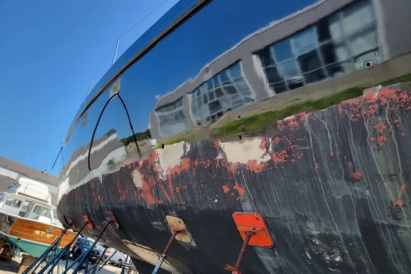 Slide: The Image of Weathered hull of a 1989 Rob Ladd PH Motorsailer Cutter, reflecting nearby buildings. - 1