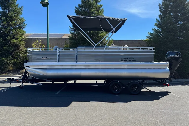 The Image of 2026 Sun Tracker Fishin' Barge 22 DLX pontoon boat on trailer in parking lot. - 0
