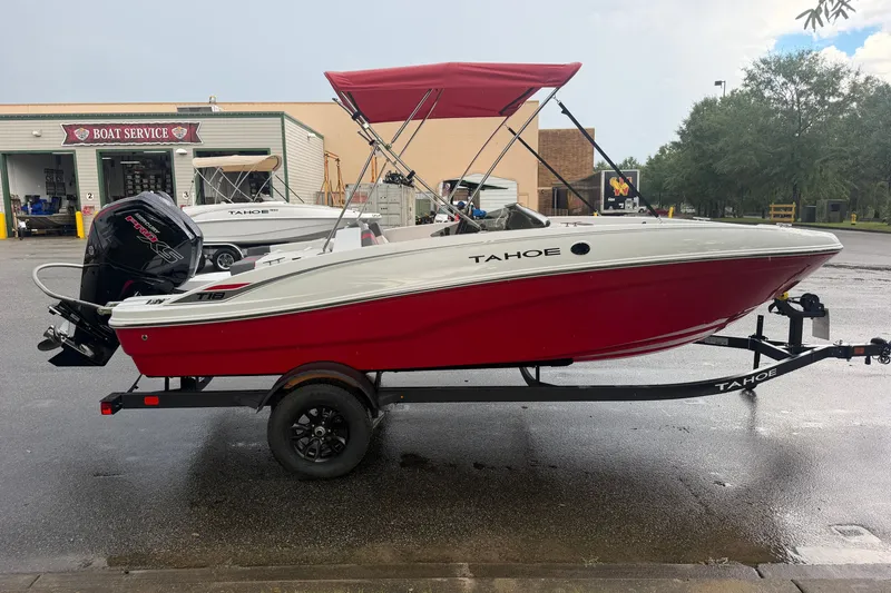 Slide: The Image of 2027 Tahoe T18 boat with red hull on trailer, parked near boat service center. - 2
