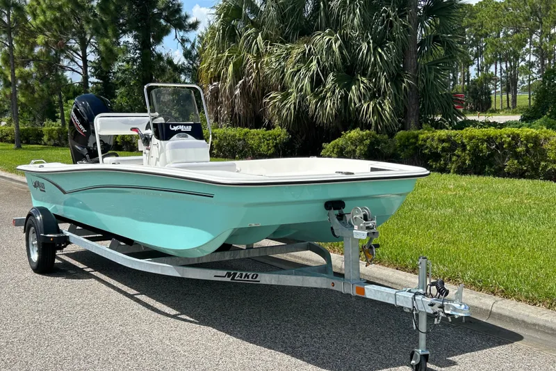 Slide: The Image of 2027 Mako Pro Skiff 17 CC boat on trailer, parked near lush greenery. - 1
