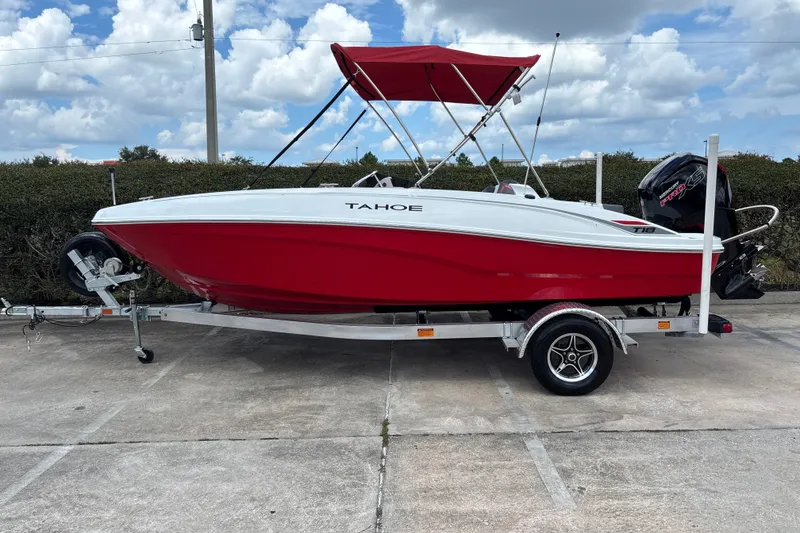 The Image of 2027 Tahoe T18 boat with red hull and canopy on trailer, parked outdoors. - 0