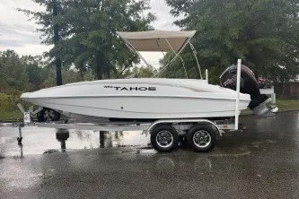 The Image of 2027 Tahoe 1950 boat on trailer, parked on wet pavement with trees in background. - 0