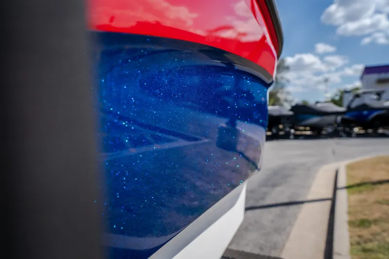 Slide: The Image of 2020 MasterCraft X26 boat with sparkling blue and red hull, parked outdoors. - 11