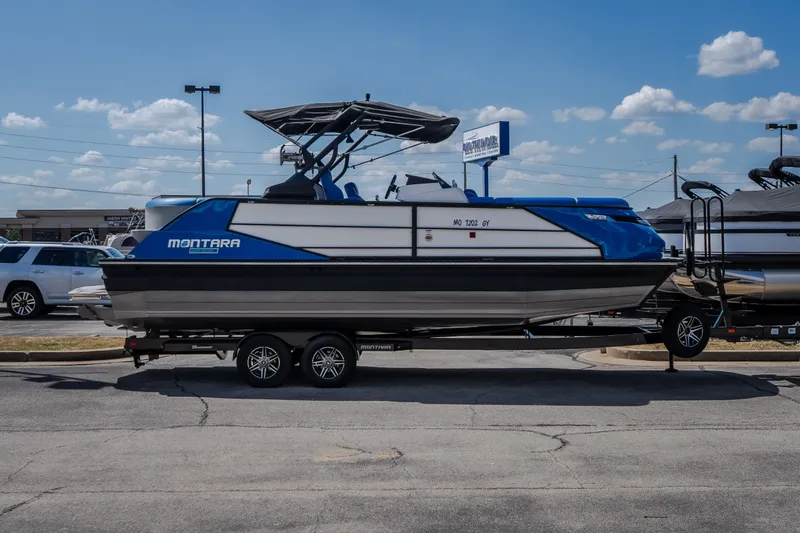 Slide: The Image of 2025 Montara 25 Surf Boss boat on trailer, blue and white design, parked outdoors. - 10