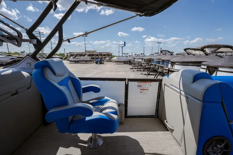 Slide: The Image of 2025 Montara 25 Surf Boss boat interior with blue seating, parked at a dealership under a clear sky. - 33