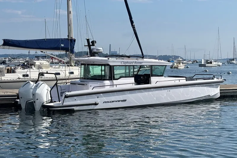 The Image of 2024 Axopar 37 XC Cross Cabin boat docked in a marina, surrounded by sailboats. - 0