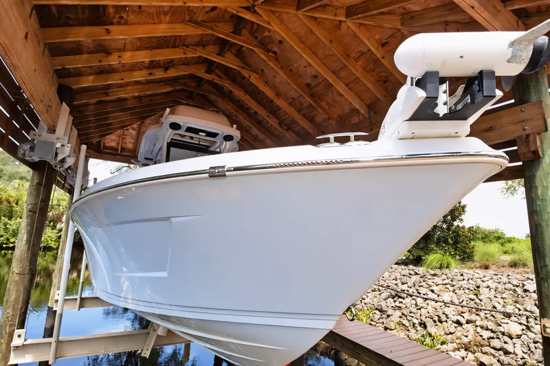 Slide: The Image of 2021 Blue Wave 2800 Makaira boat under wooden shelter, docked by a rocky shoreline. - 3