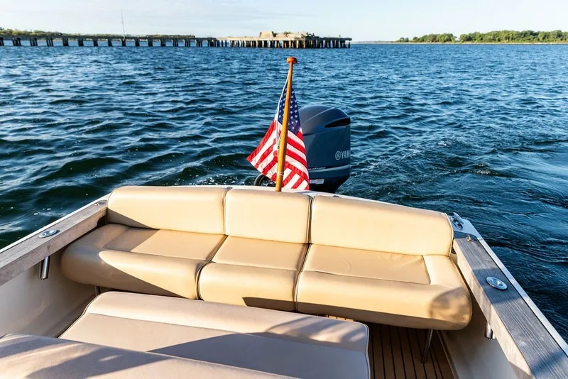 Slide: The Image of 2018 Hunt Yachts Harrier 26 on water, featuring beige seating and American flag. - 18