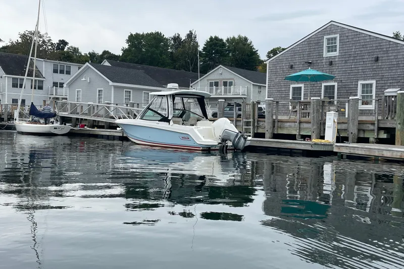 Slide: The Image of 2023 Boston Whaler 240 Vantage docked at a marina with coastal homes in the background. - 32