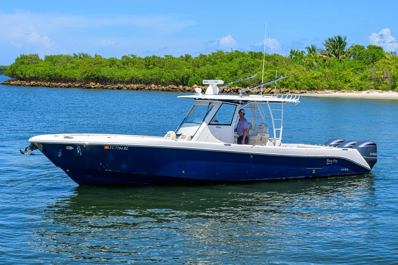 The Image of 2018 Everglades 355 Center Console boat on calm water near a lush shoreline. - 0