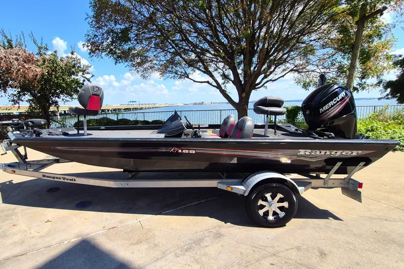 Slide: The Image of 2019 Ranger RT188 boat on trailer, parked near waterfront under a tree. - 0