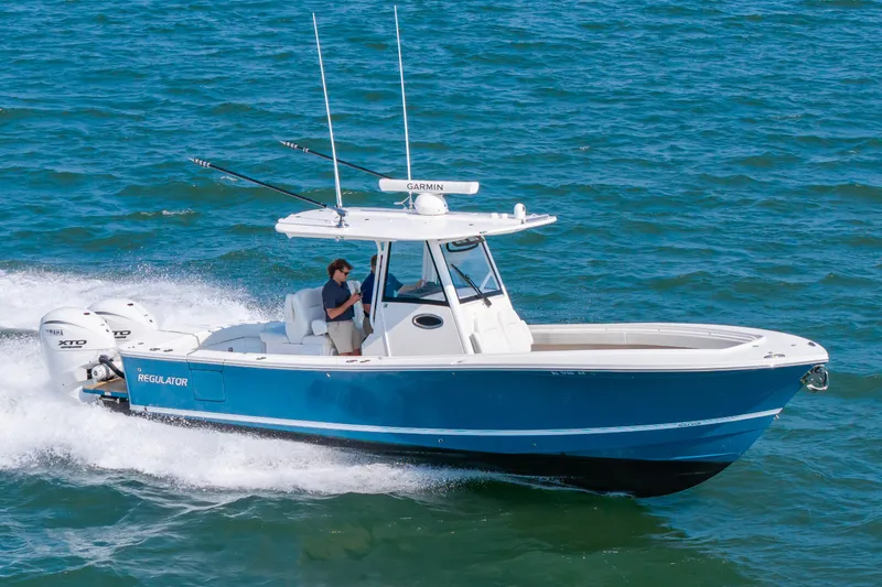 Slide: The Image of A 2024 Regulator 31 boat speeds across the water. It features a blue hull and twin outboard engines. - 24