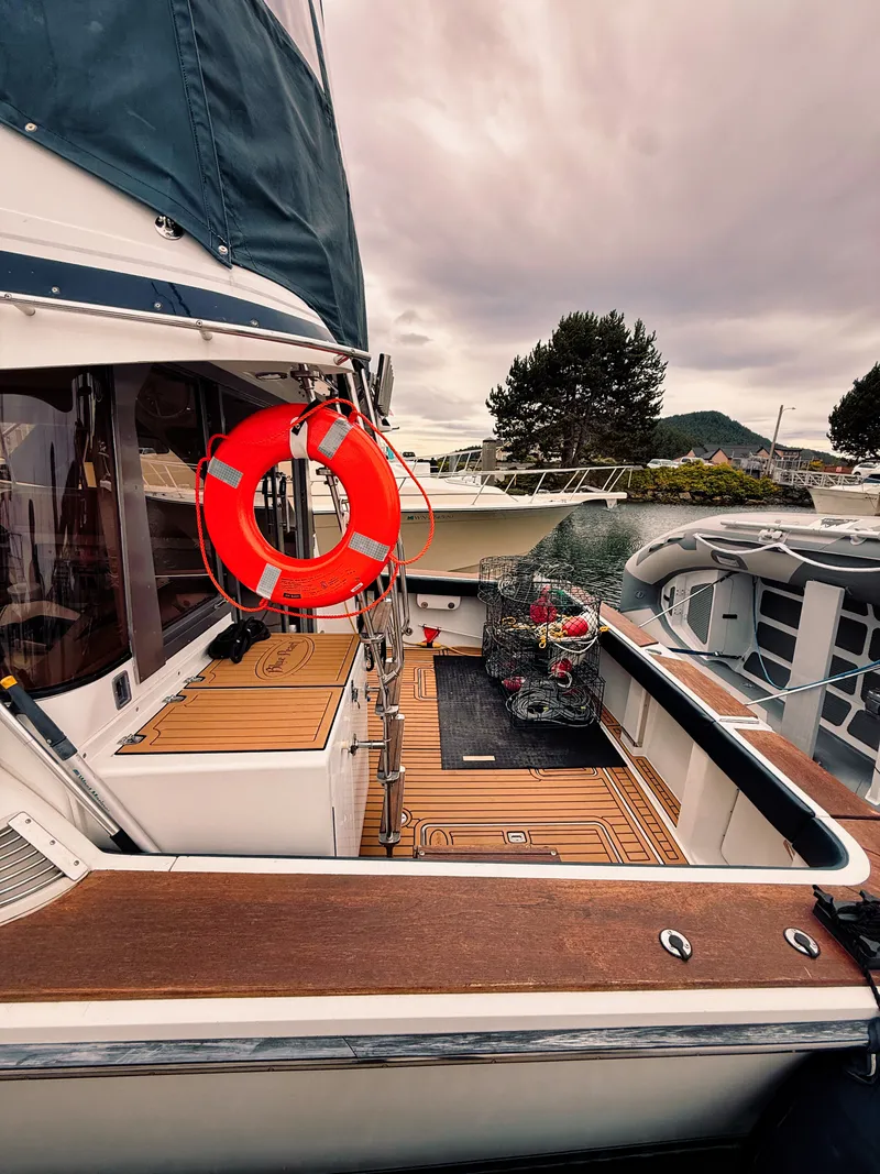 Slide: The Image of A 1987 Trojan International 10.8 Meter Sedan with wooden deck and lifebuoy, docked at a marina. - 15