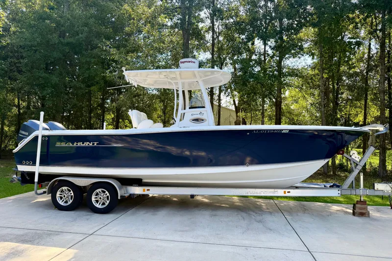 Slide: The Image of 2013 Sea Hunt Gamefish 27 boat on trailer, parked outdoors with forest background. - 2