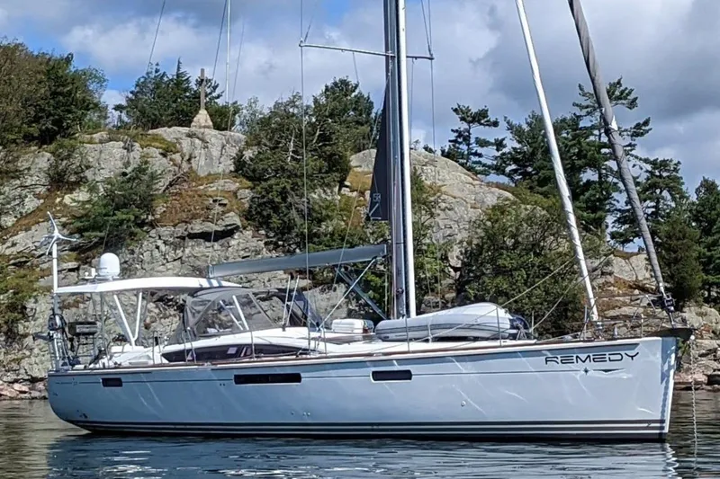 The Image of 2012 Jeanneau 57 sailboat named "Remedy" anchored near rocky shoreline. - 0